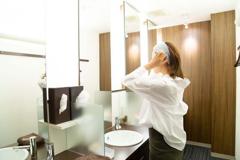 鏡の前でニキビをメイクで隠そうとする女性