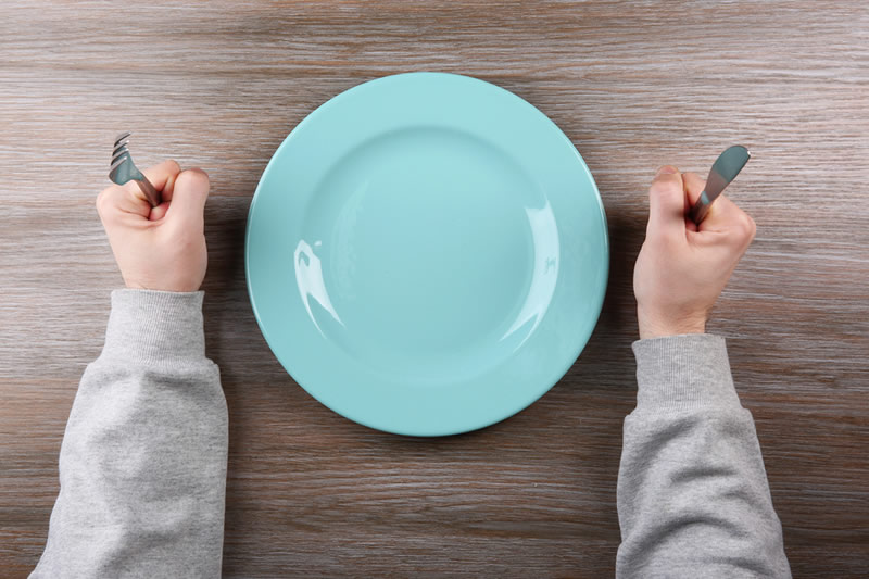 空腹の女性が皿の前で食事を待っているところ