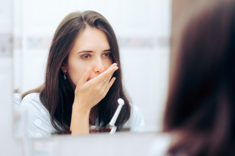 鏡を見て口の中の歯周病を気にする女性