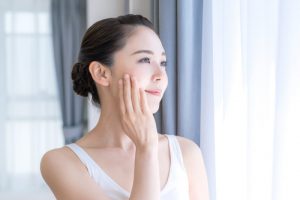 手でほほを触りながら外を見ている女性
