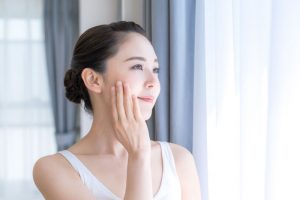 窓を見てシミを気にする20代の女性