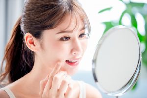 鏡で頬の肌を確かめている女性