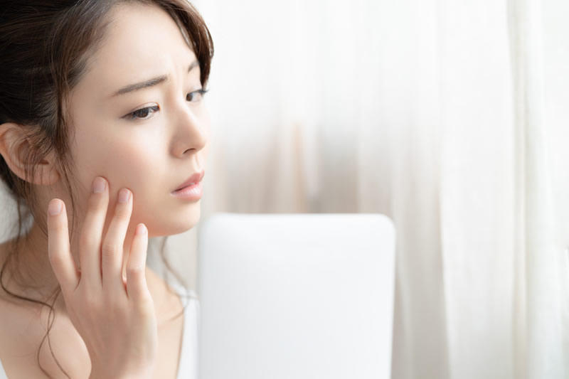 鏡ではだのたるみを確認している女性