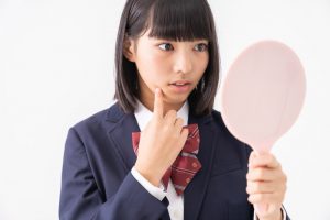 鏡を見てニキビを気にする女子高生