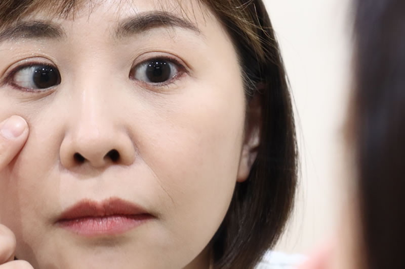鏡でまぶたのラインを確かめる女性