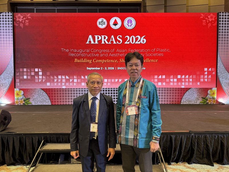 APRAS 2026の看板の前で海外の形成外科医と写る水野博司医師