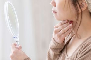 鏡を見ながらあごの下に手を当てている女性