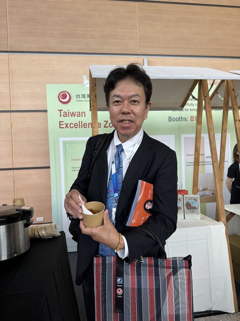 OSAPS 2026の会場の展示エリアで、カップを手にする水野博司医師
