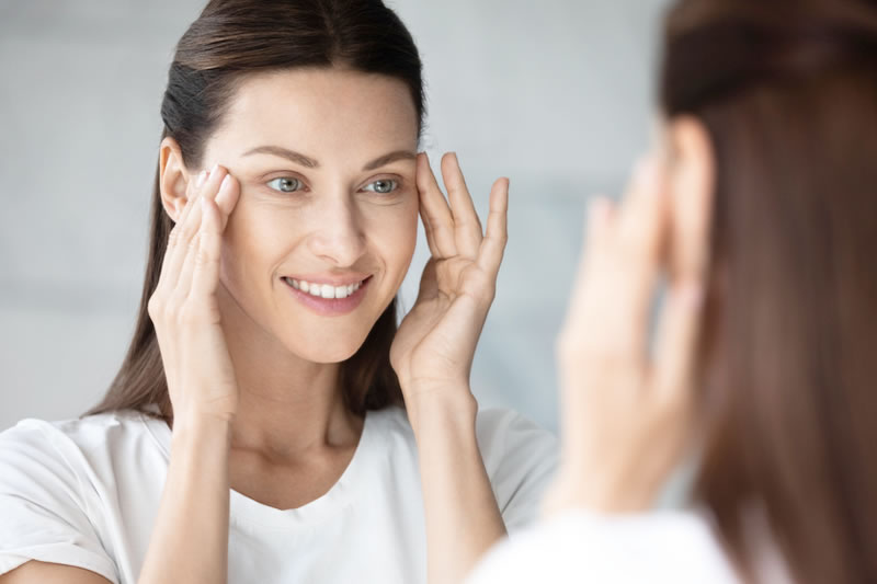 目の下のたるみを気にして鏡を見ている女性